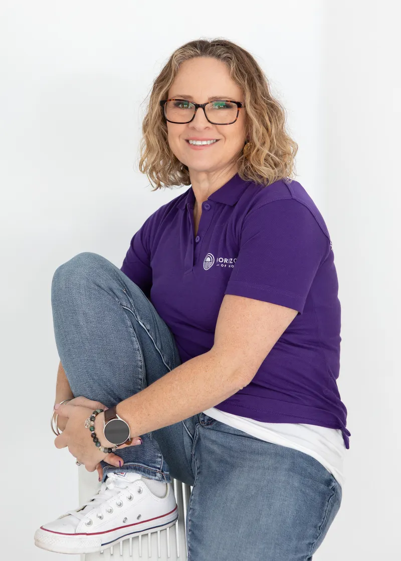 A woman in a purple shirt and glasses sits on a stool, exuding warmth and understanding, dedicated to helping families navigate challenges_11zon
